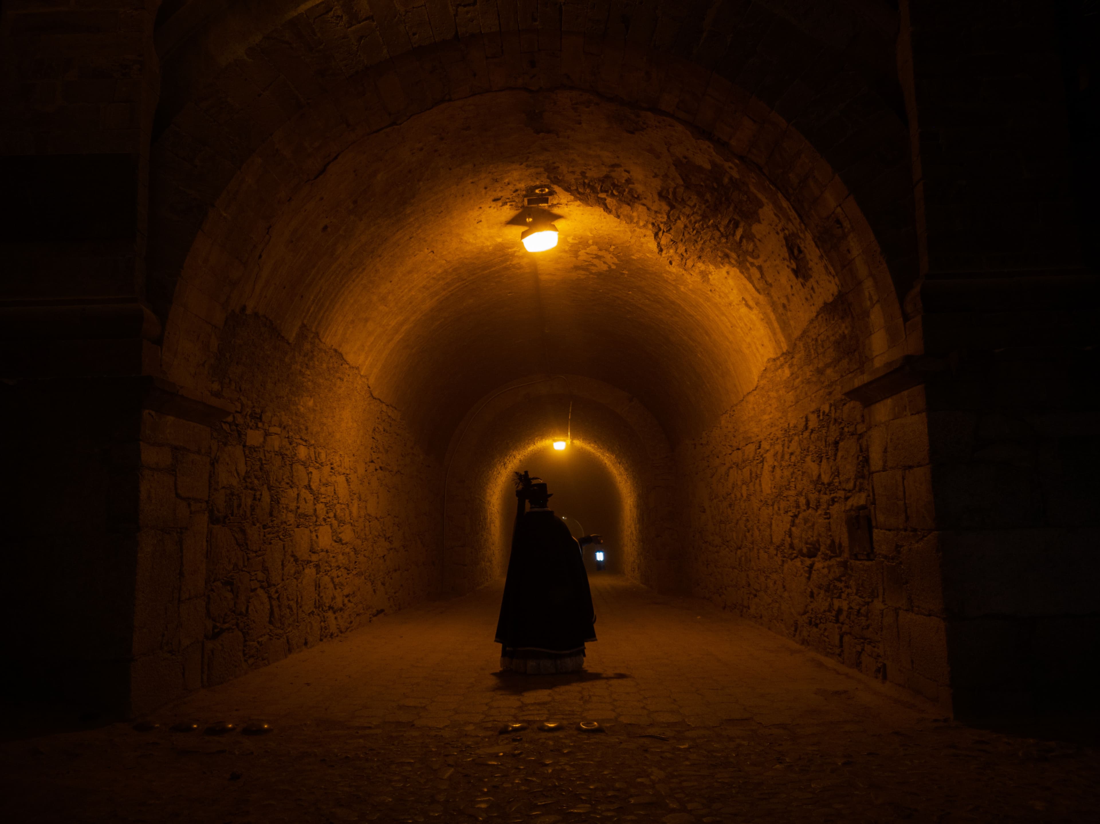 Solitary cloaked figure in a candlelit gothic arched hall — photo by Walter Alejandro on Pexels